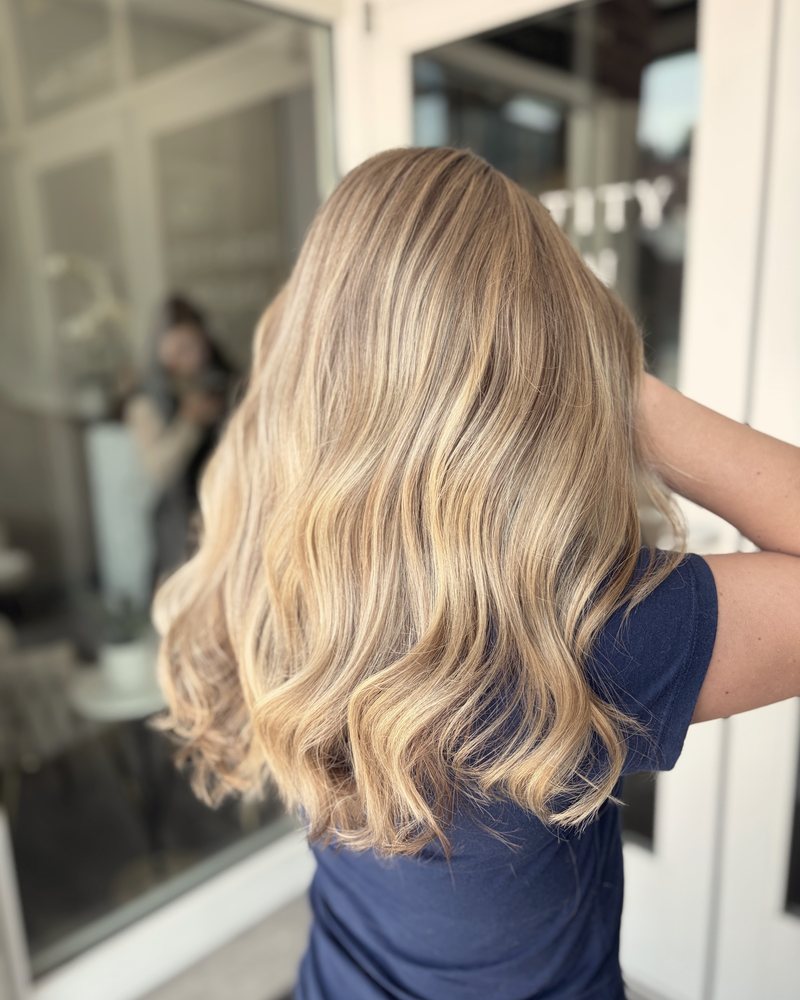 Blonde balayage seen from behind, in front of the salon doors